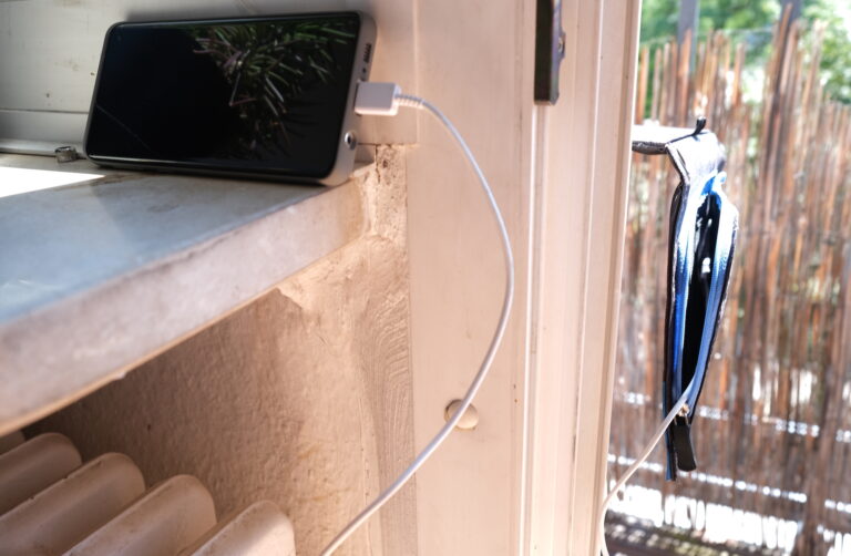 Ideal ist diese Konstruktion nicht, aber notwendig. Das Solarladegerät liegt draußen auf dem Balkon, das Smartphone, das es lädt, bleibt drinnen auf der Fensterbank halbwegs kühl.