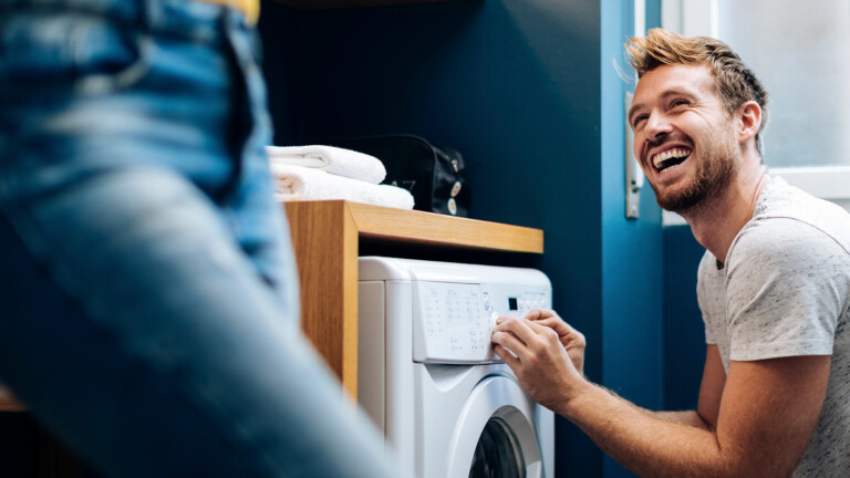 Lachender Mann vor Waschmaschine