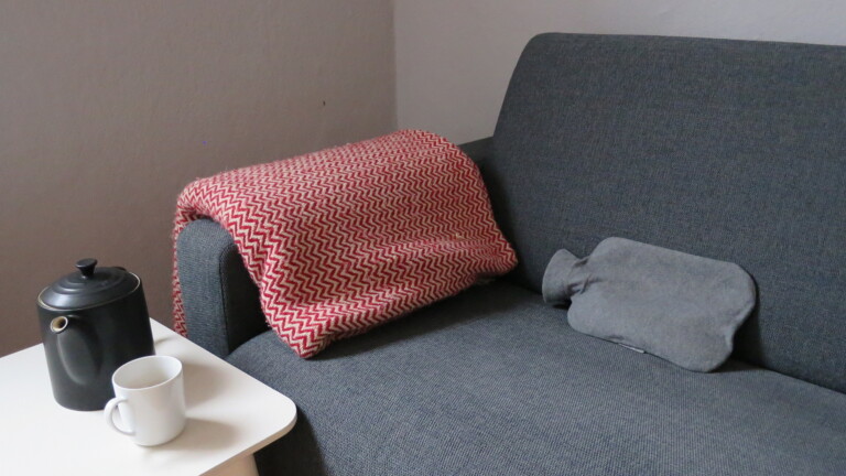 Sofa mit Decke, Wärmflasche und heißem Tee